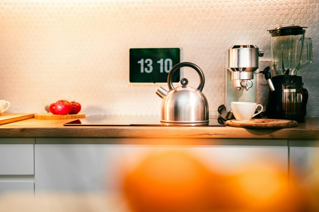 Contemporary kitchen counter with stainless kettle, coffee machine, and digital clock.